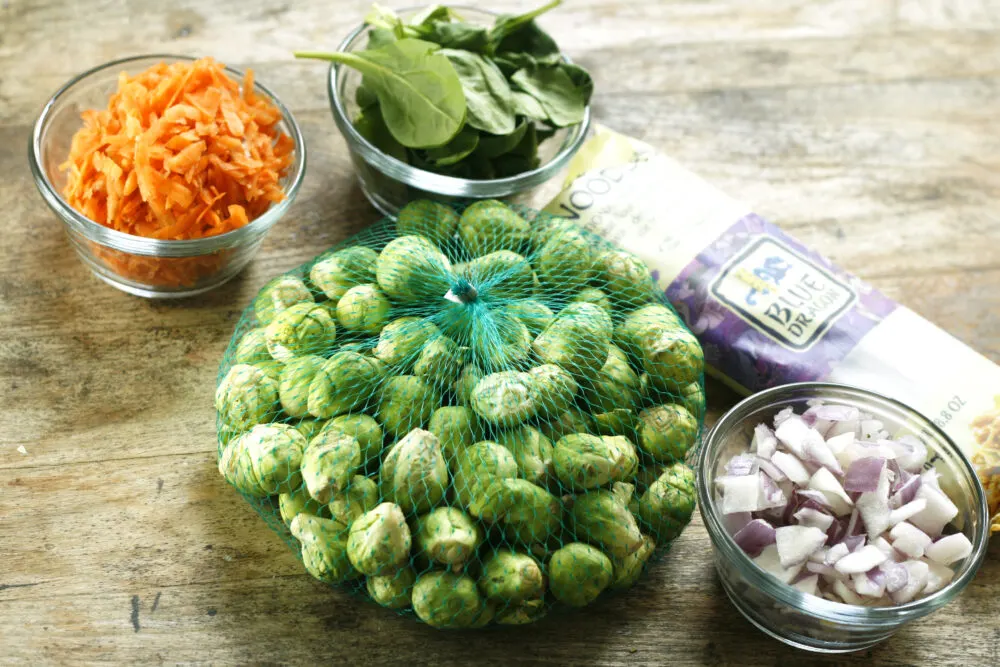 Ingredients for Sesame Soba Noodles with Brussels Sprouts are shown on a wooden table.