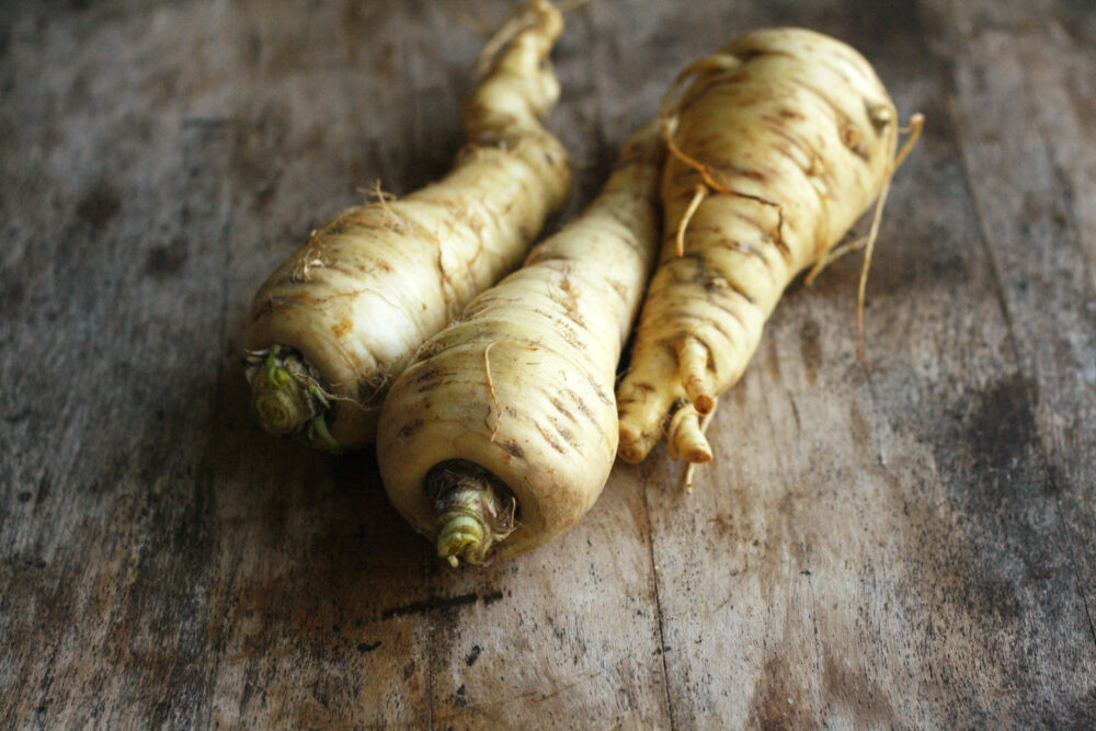 Three parsnips are shown on a wood table.