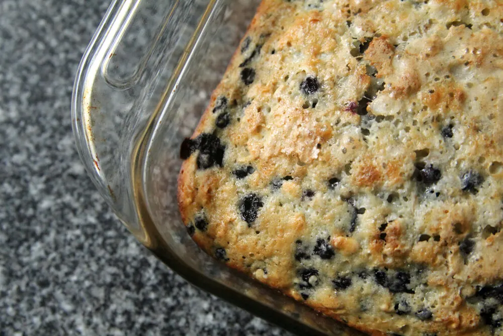 A glass baking pan holds Blueberry Oatmeal Cake on a granite countertop.