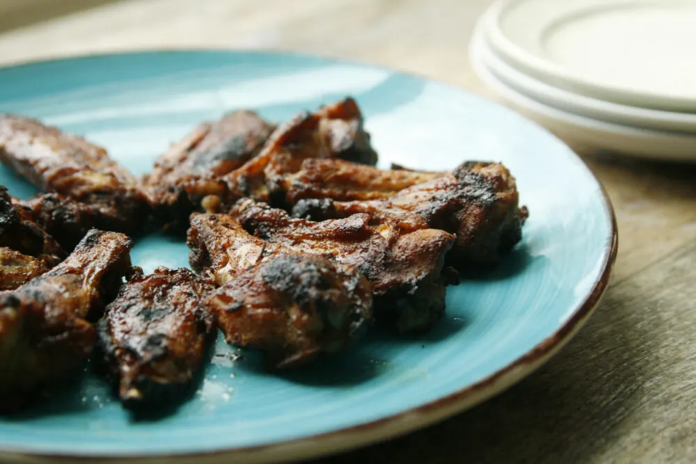 A teal plate of Slow Cooker Hoisin Chicken Wings is shown on a wooden surface with a stack of plates in the background.