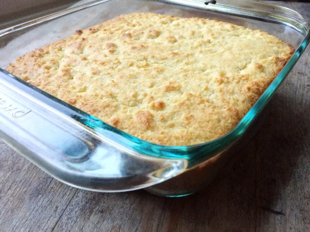 A glass pan of Buttery Cornbread is shown from the side on a wooden countertop.