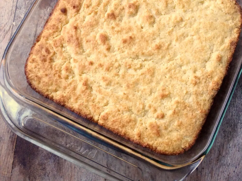 A glass pan of Buttery Cornbread is shown from above on a wooden countertop.