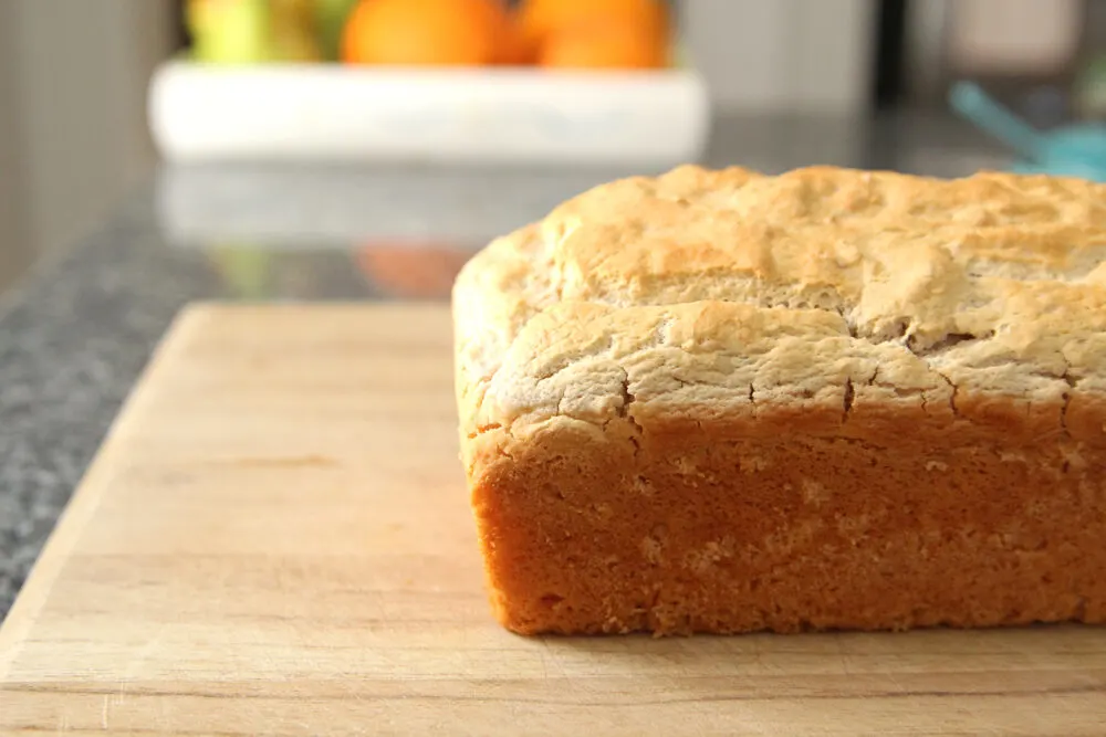 A loaf of golden brown bread sits on a cutting board on a granite countertop.