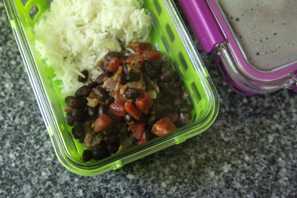 Black beans with tomatoes and onions are shown with white rice in a green meal prep container.