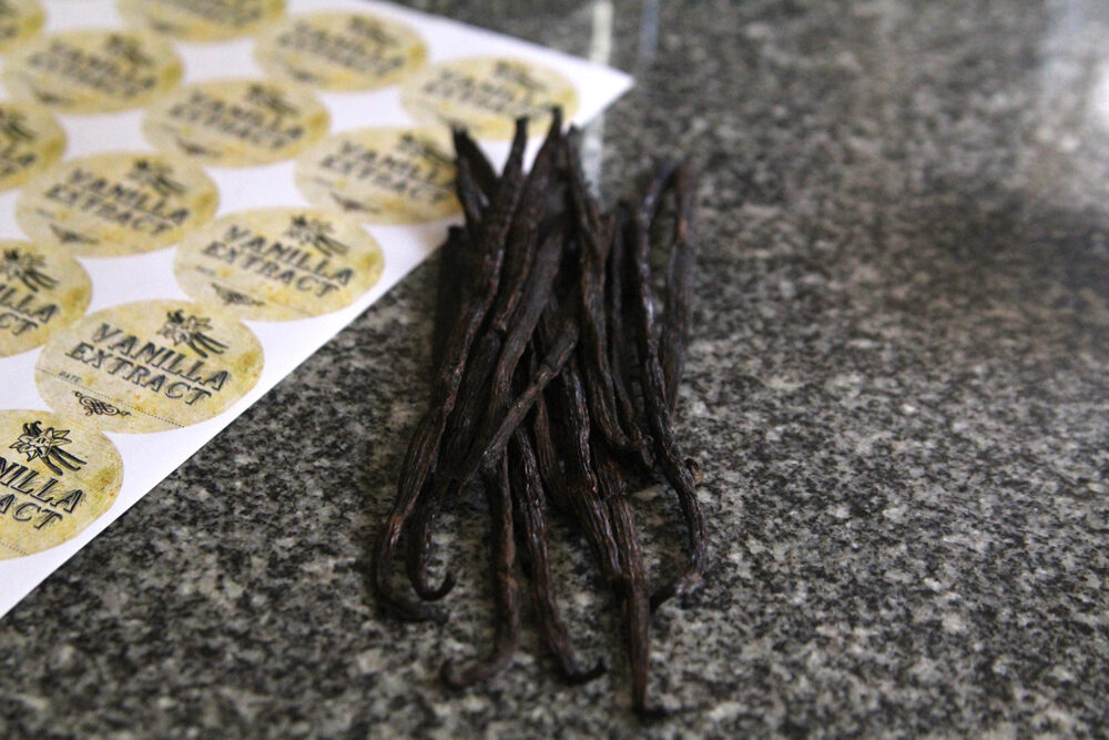 A pile of vanilla beans and a sheet of labels sit on a counter.