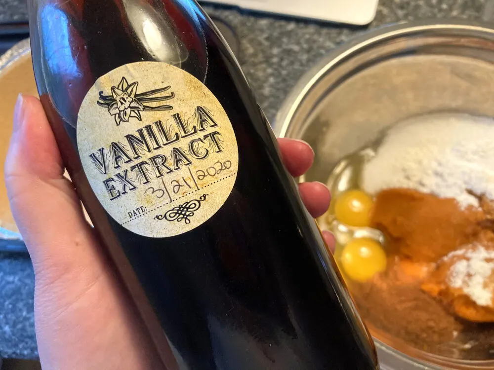 A bottle of vanilla extract is held in a hand over a mixing bowl.