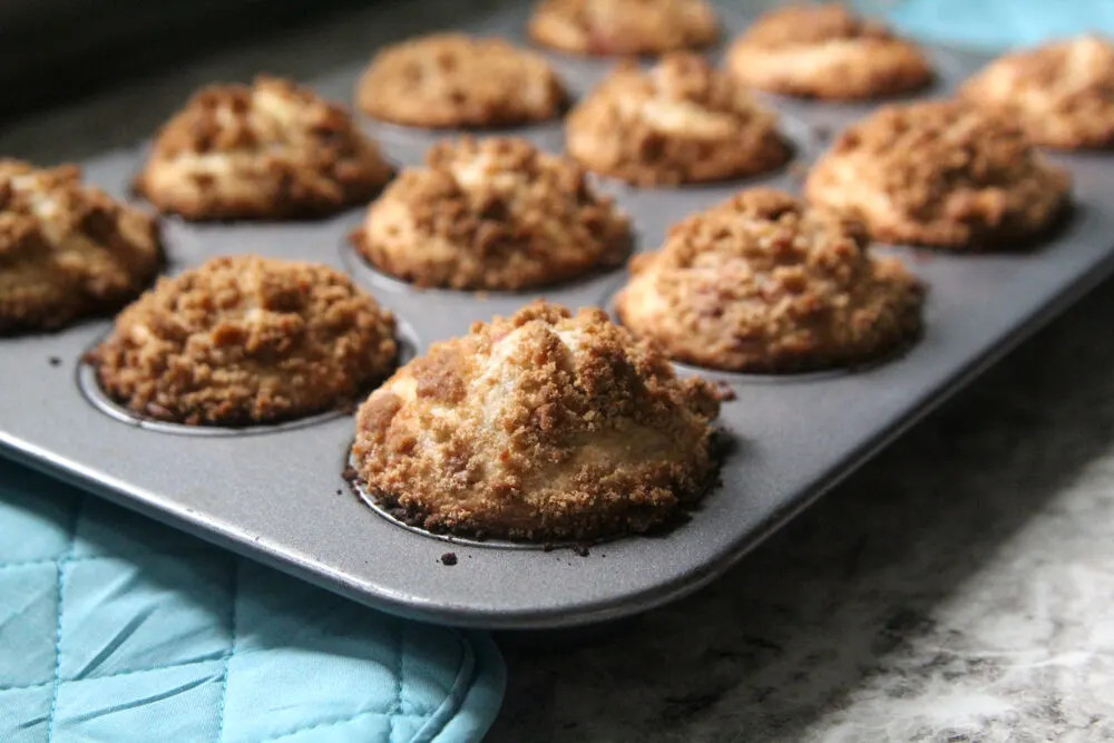 A muffin pan is filled with freshly baked Raspberry Streusel Muffins on a countertop.