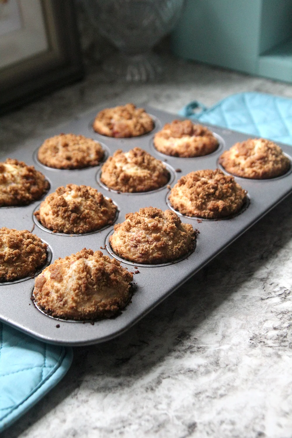 A muffin pan filled with Raspberry Streusel Muffins sits on a countertop.
