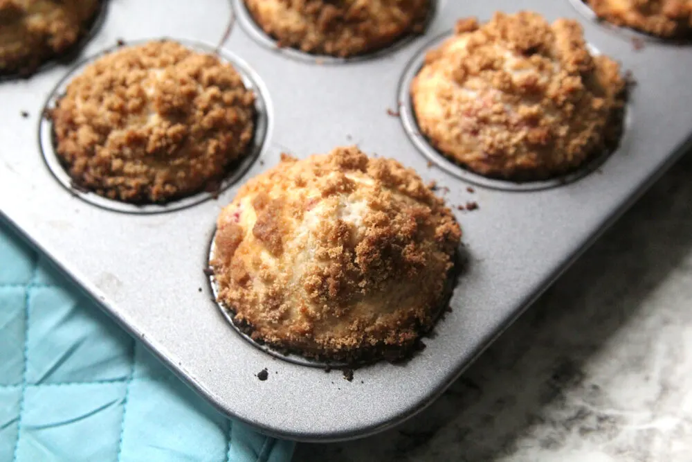 Raspberry Streusel Muffins sit in a muffin pan on a counter, hot from the oven.