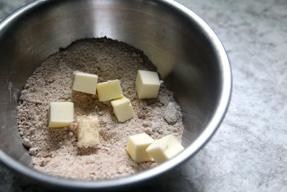 A silver bowl holds a beige mixture with cubes of butter on top.