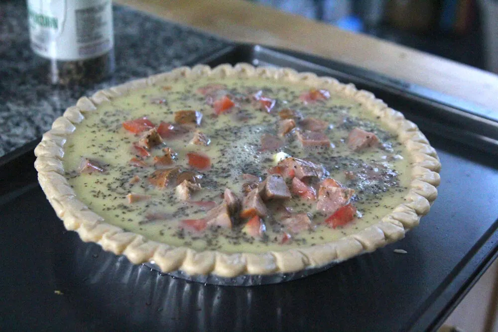 A raw quiche with sausage, tomato and cheese sits on a baking sheet, waiting to go into the oven.