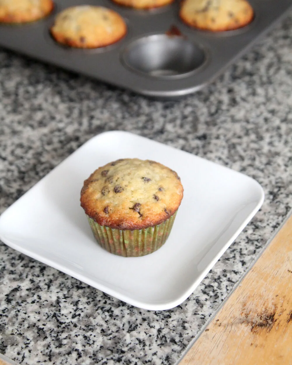 A banana chocolate chip muffin sits on a white plate on a granite countertop.