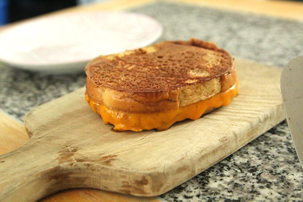 A grilled cheese sandwich is shown on a wooden cutting board.