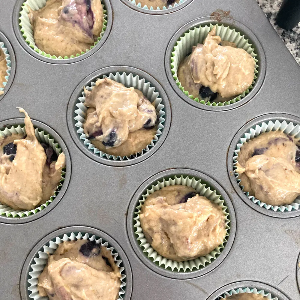 A muffin tin is filled with muffin cups with batter inside.