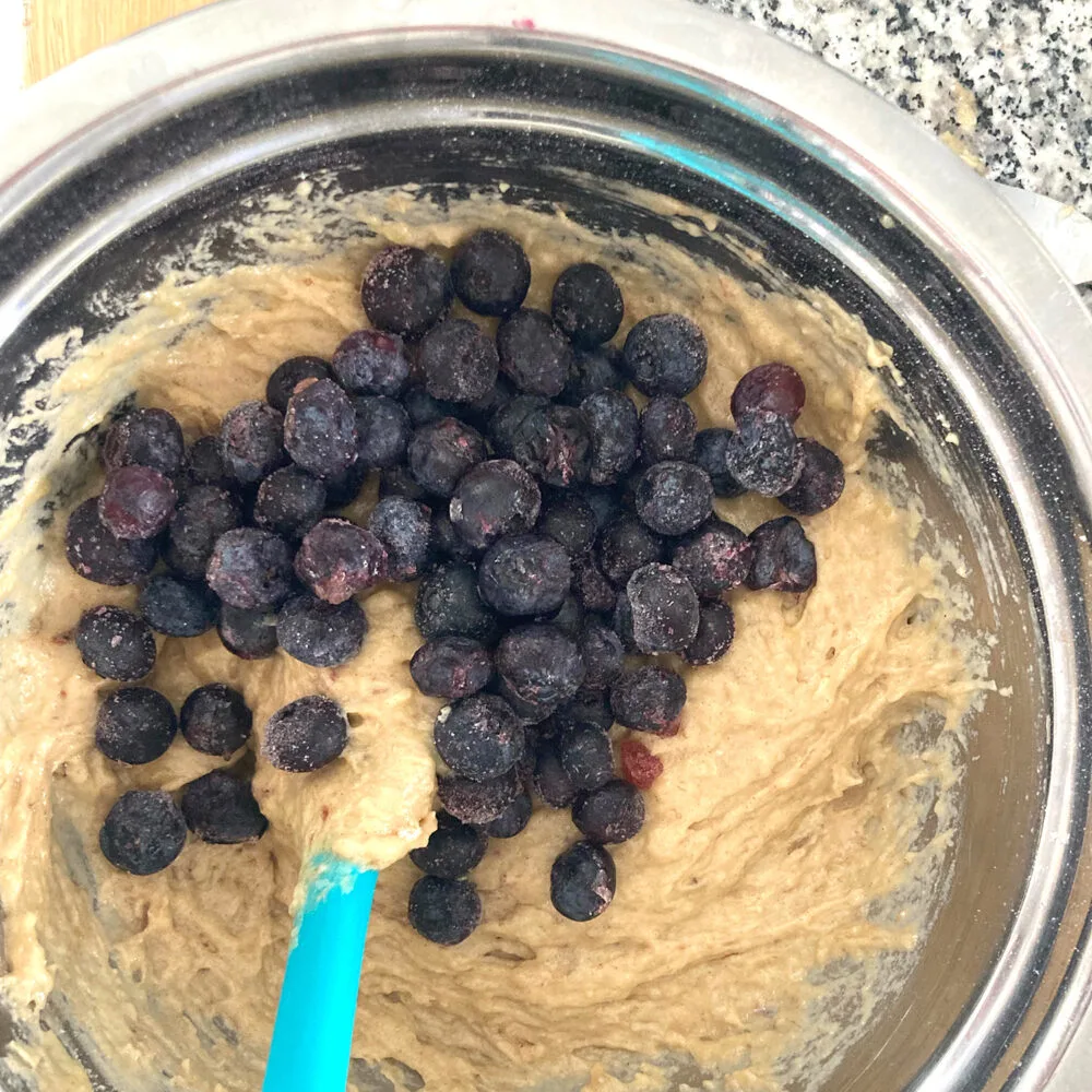 A silver bowl filled with batter is topped with blueberries.