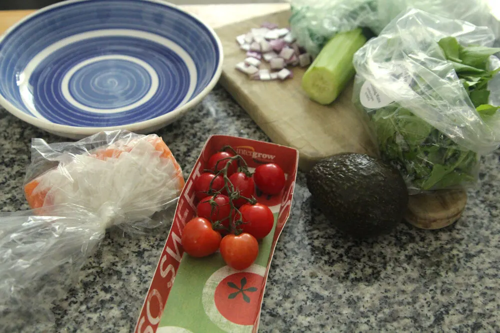Ingredients for a salad are spread out on a counter. A blue bowl sits nearby.