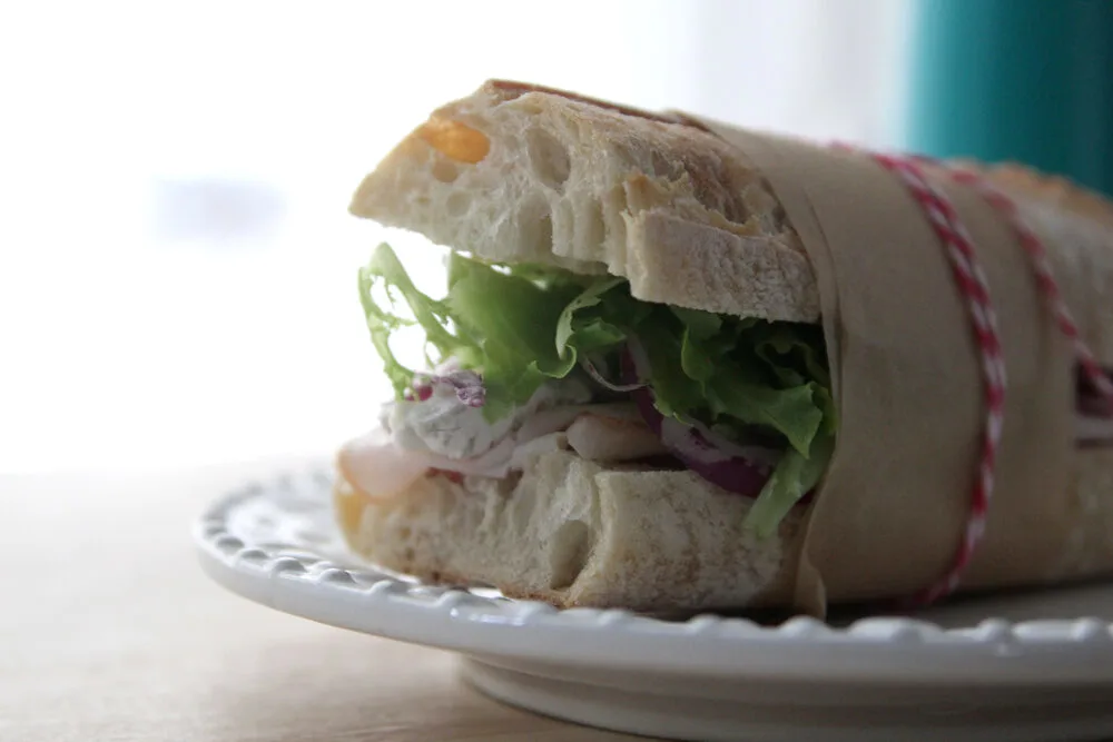 A sandwich is shown on a white plate. Turkey, red onion, green lettuce and brie are visible. 