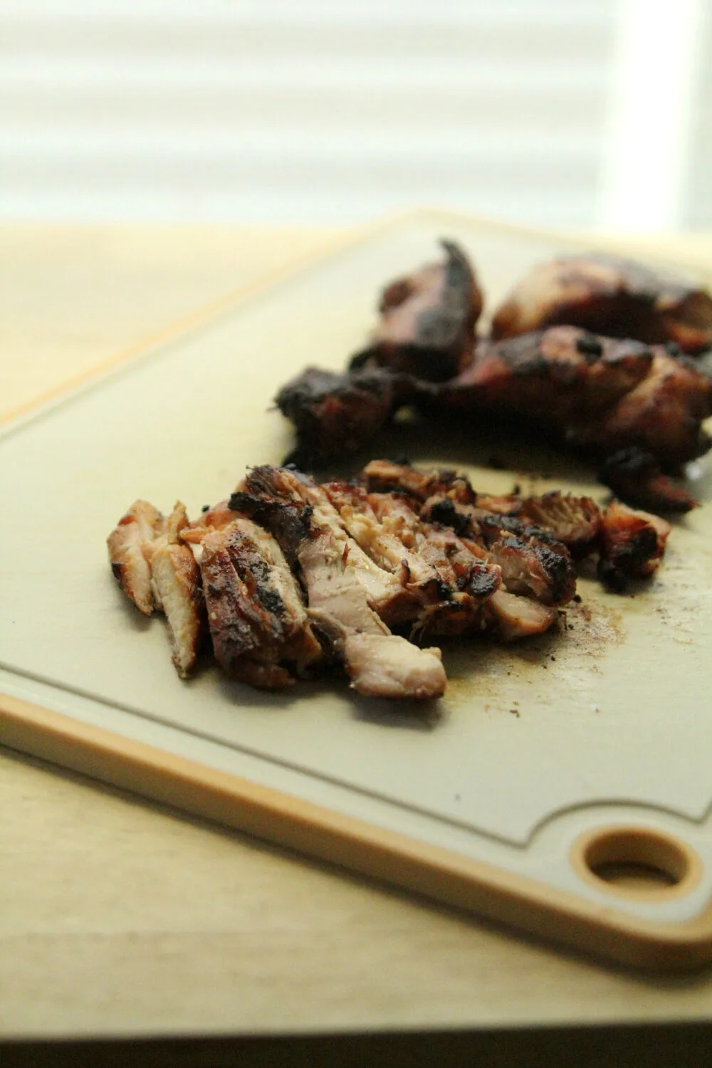 Sliced grilled bourbon chicken thighs are shown on a cutting board.