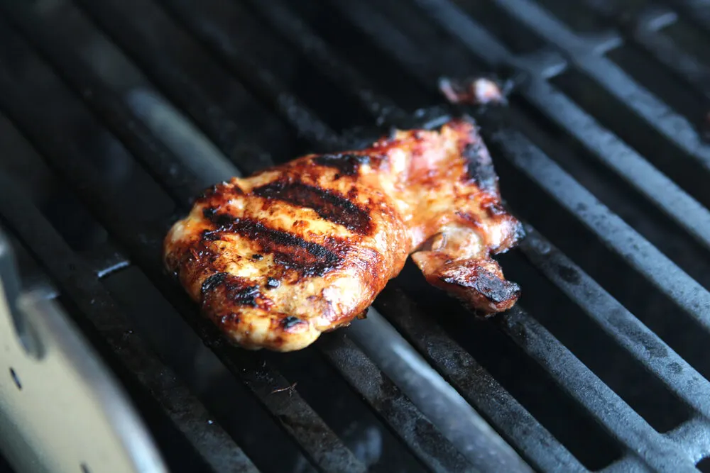 A grilled bourbon chicken thigh is shown on a grill. It's browned and golden with grill marks.