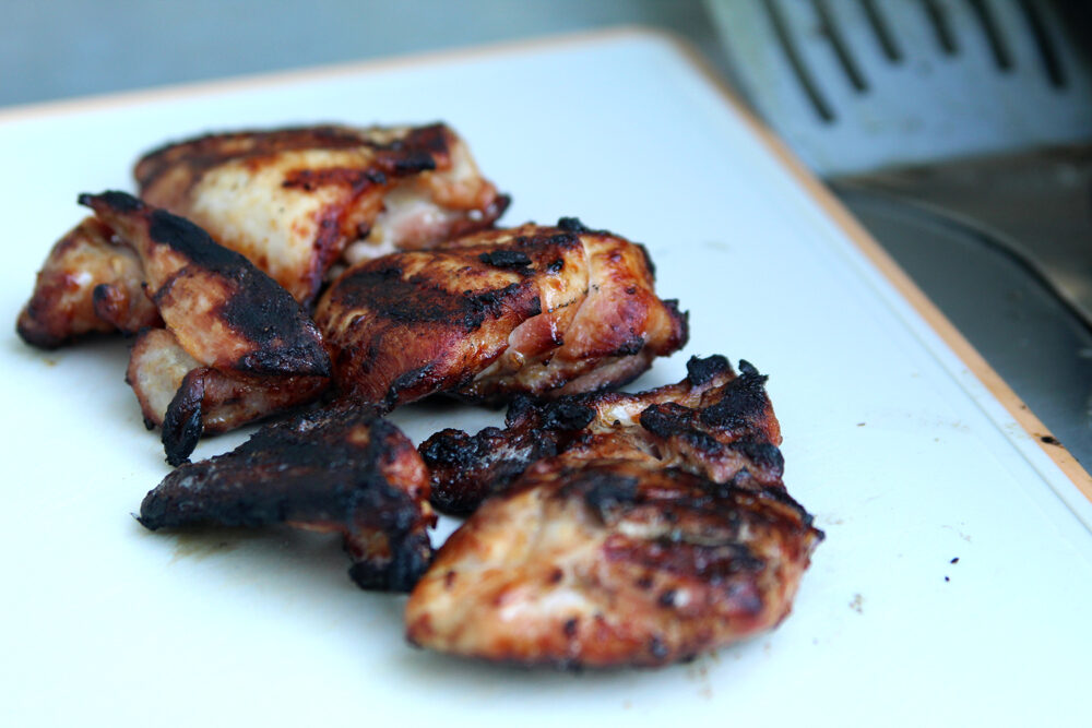 Grilled chicken thighs are shown on a cutting board. They are browned and have grill marks.