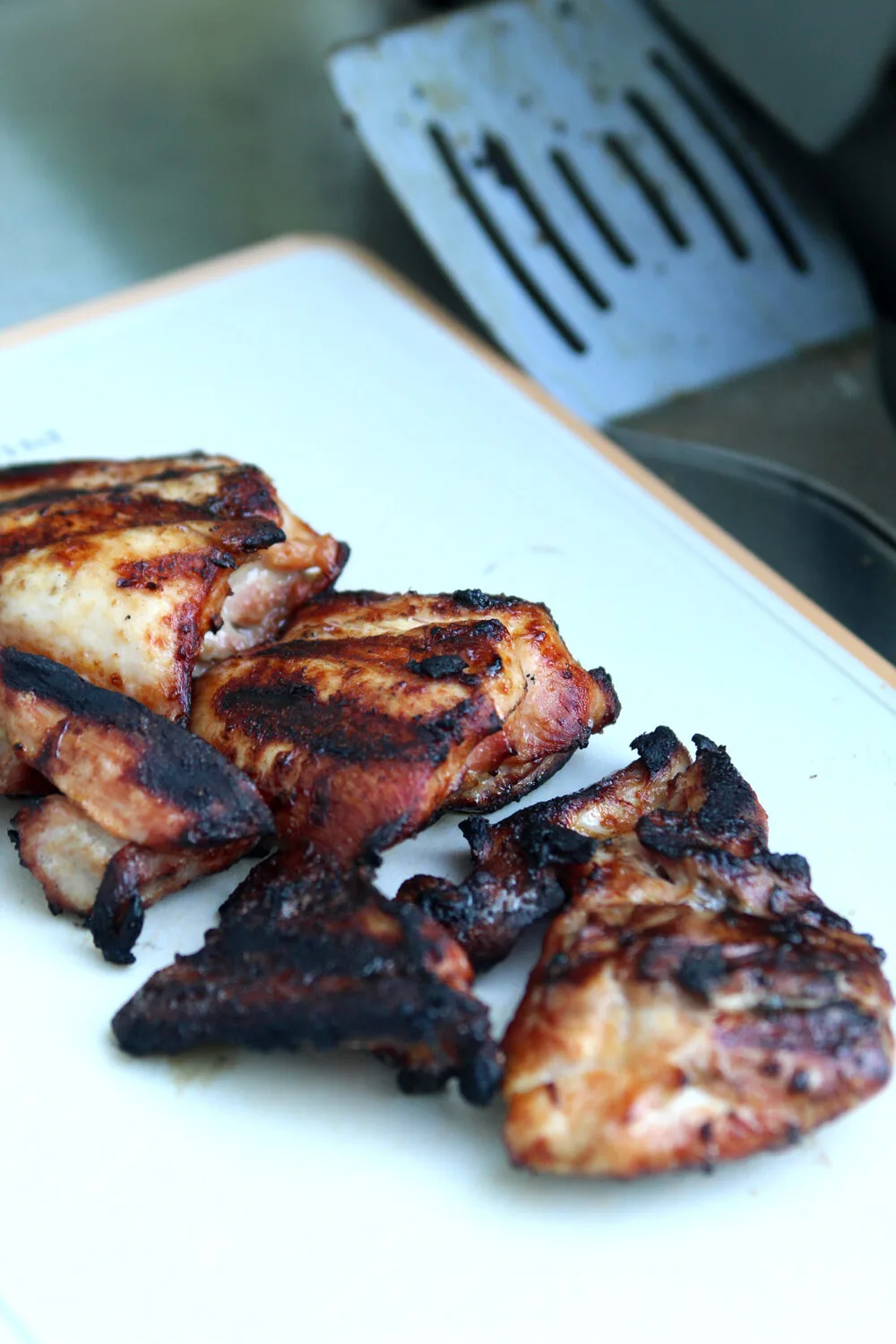 Cooked chicken thighs are shown on a cutting board. They are browned and golden and a reddish color with grill marks.