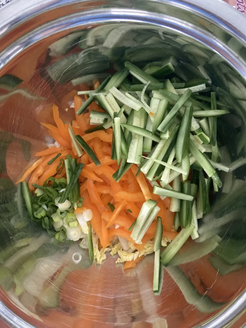 Julienne cut veggies in greens and orange are shown in a metal mixing bowl