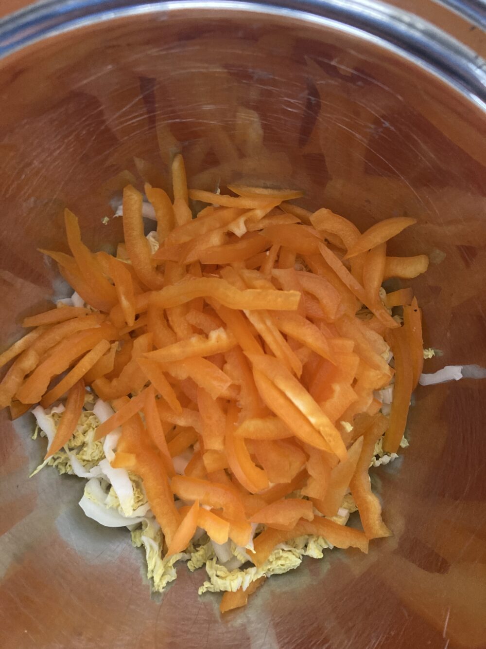 Thinly sliced orange sweet bell pepper is seen in a metal mixing bowl.