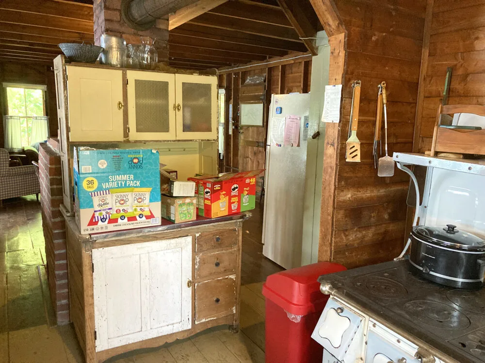 The inside of a rustic cabin is seen. A hutch has boxes of popcorn and chips on it.