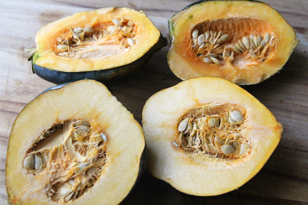 Four halves of acorn squash are shown in a wooden cutting board, cut side up. The flesh is orange.